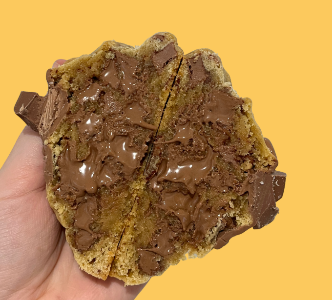 Hand held cross-section of a melty chocolate chip cookie on a yellow background